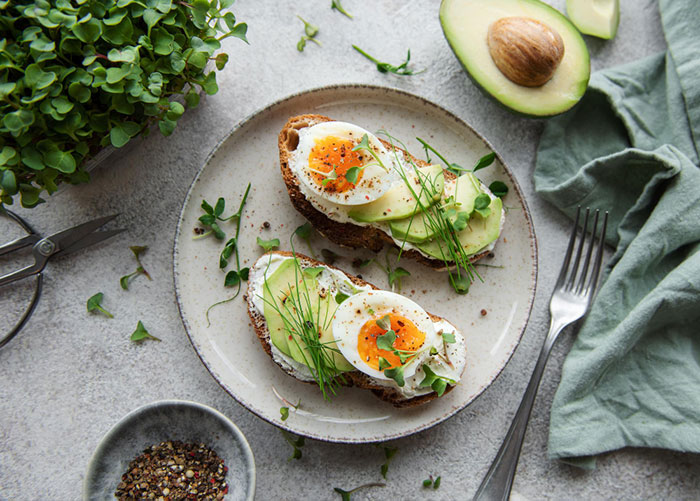 Tost sa poširanim jajetom i avokadom, ukrašen začinskim biljem, savršen recept od 250 kcal za doručak ili užinu.
